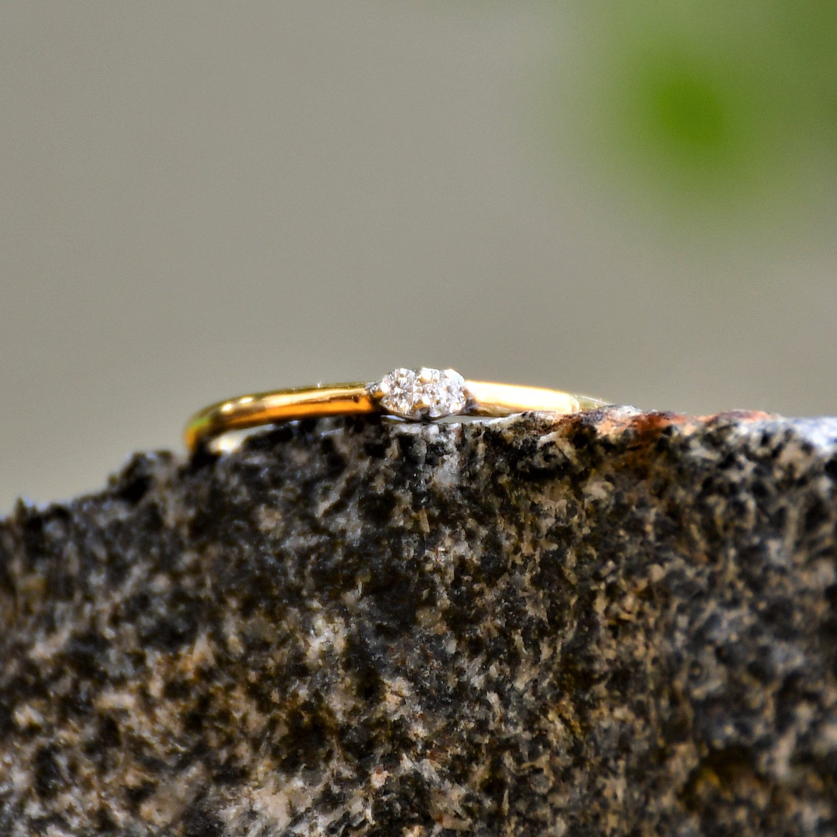 A gold band ring with two diamonds set on top, positioned on a textured dark stone surface.