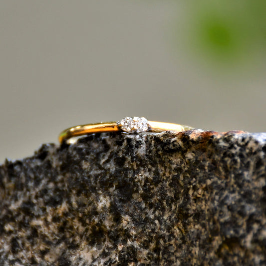 A gold band ring with two diamonds set on top, positioned on a textured dark stone surface.