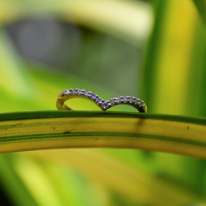 A gold ring featuring a V-shaped diamonds centerpiece, set on a green-yellow leaf surface with a blurred green background.