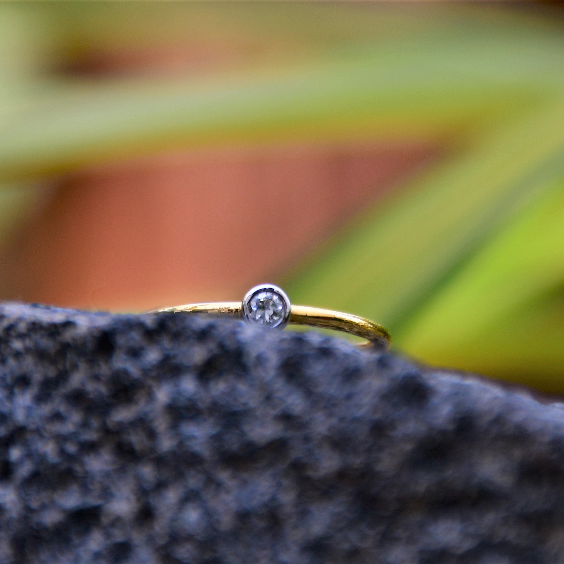A gold band ring with a single diamond set in a solitaire setting, positioned on a dark stone surface.