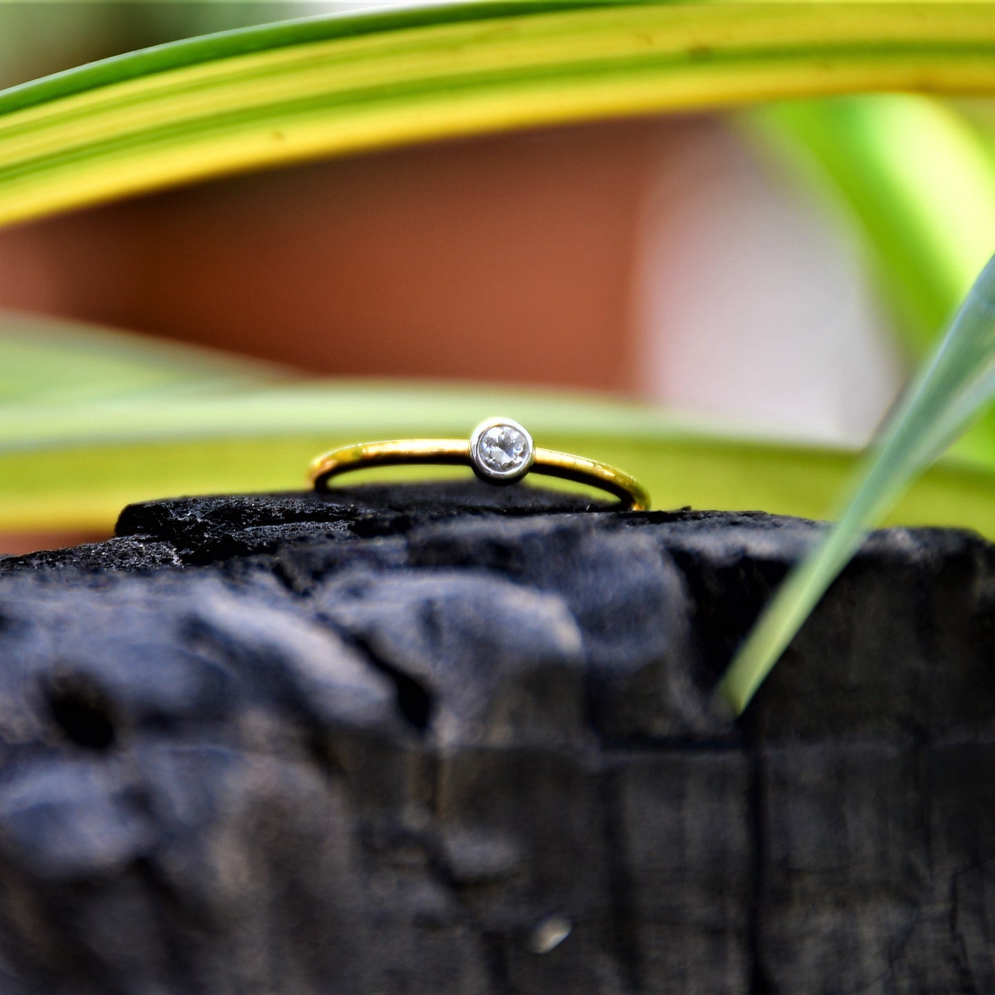 A gold band ring with a single diamond set in a solitaire setting, positioned on a dark stone surface.