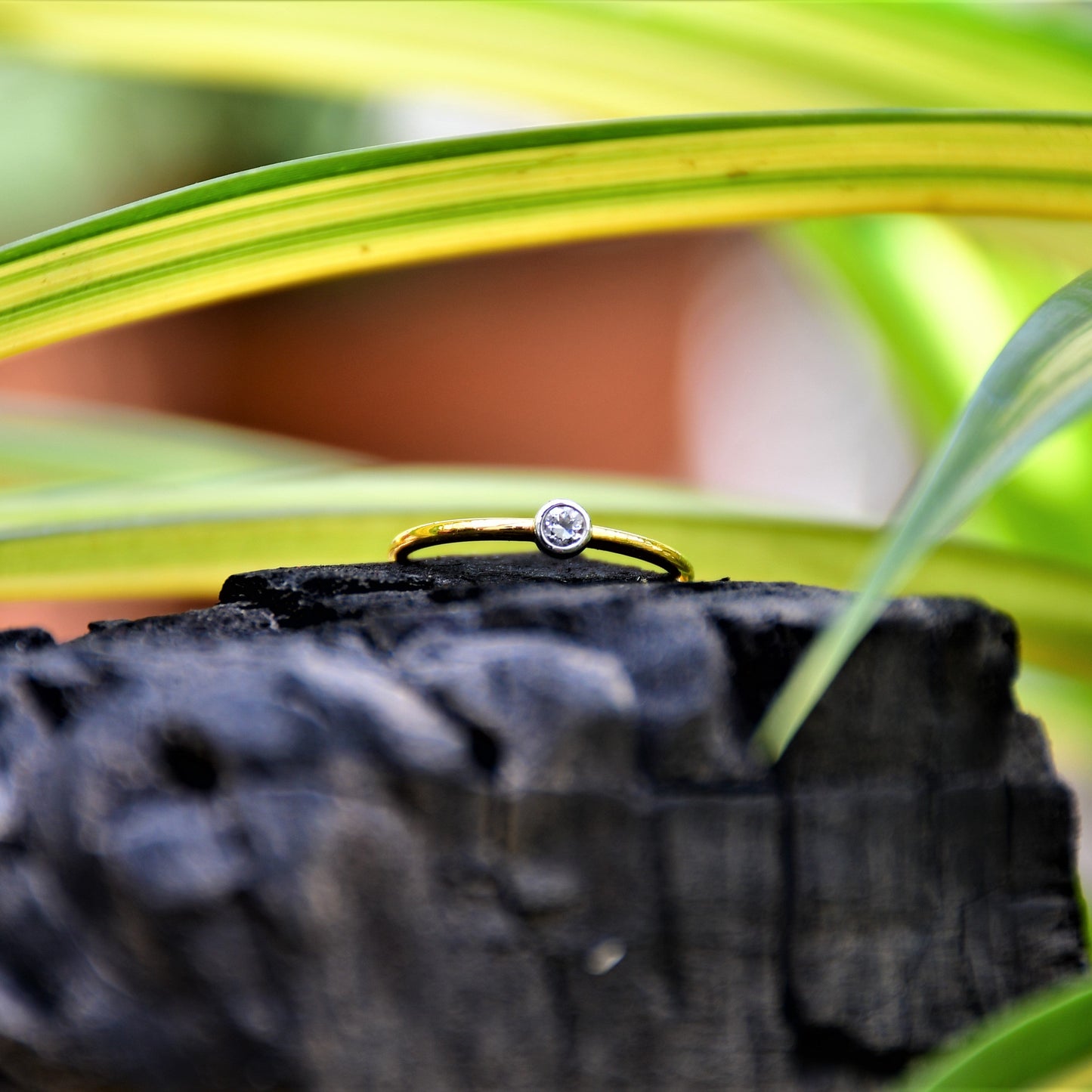 A gold band ring with a single diamond set in a solitaire setting, positioned on a dark stone surface.