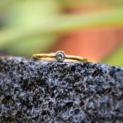 A gold band ring with a single diamond set in a solitaire setting, positioned on a dark stone surface.