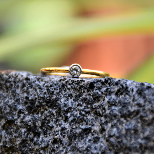 A gold band ring with a single diamond set in a solitaire setting, positioned on a dark stone surface.