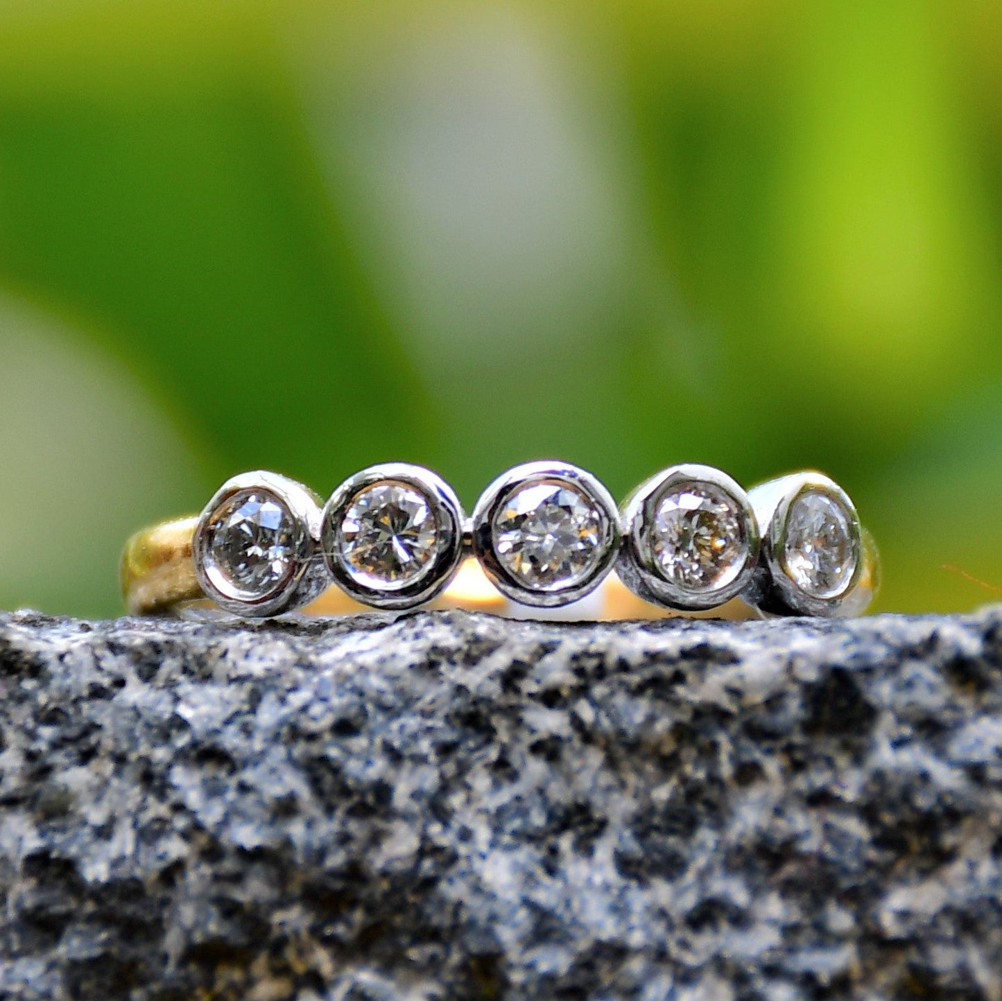 A yellow gold band ring with a series of set diamonds, featuring smaller diamonds, all set in a solid gold band displayed on a black and grey rough surface.