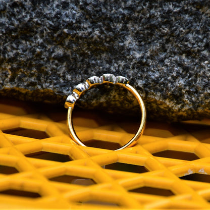 A yellow gold band ring with a series of set diamonds, featuring smaller diamonds, all set in a solid gold band, displayed on a yellow color surface and againgst a black and grey rough background.