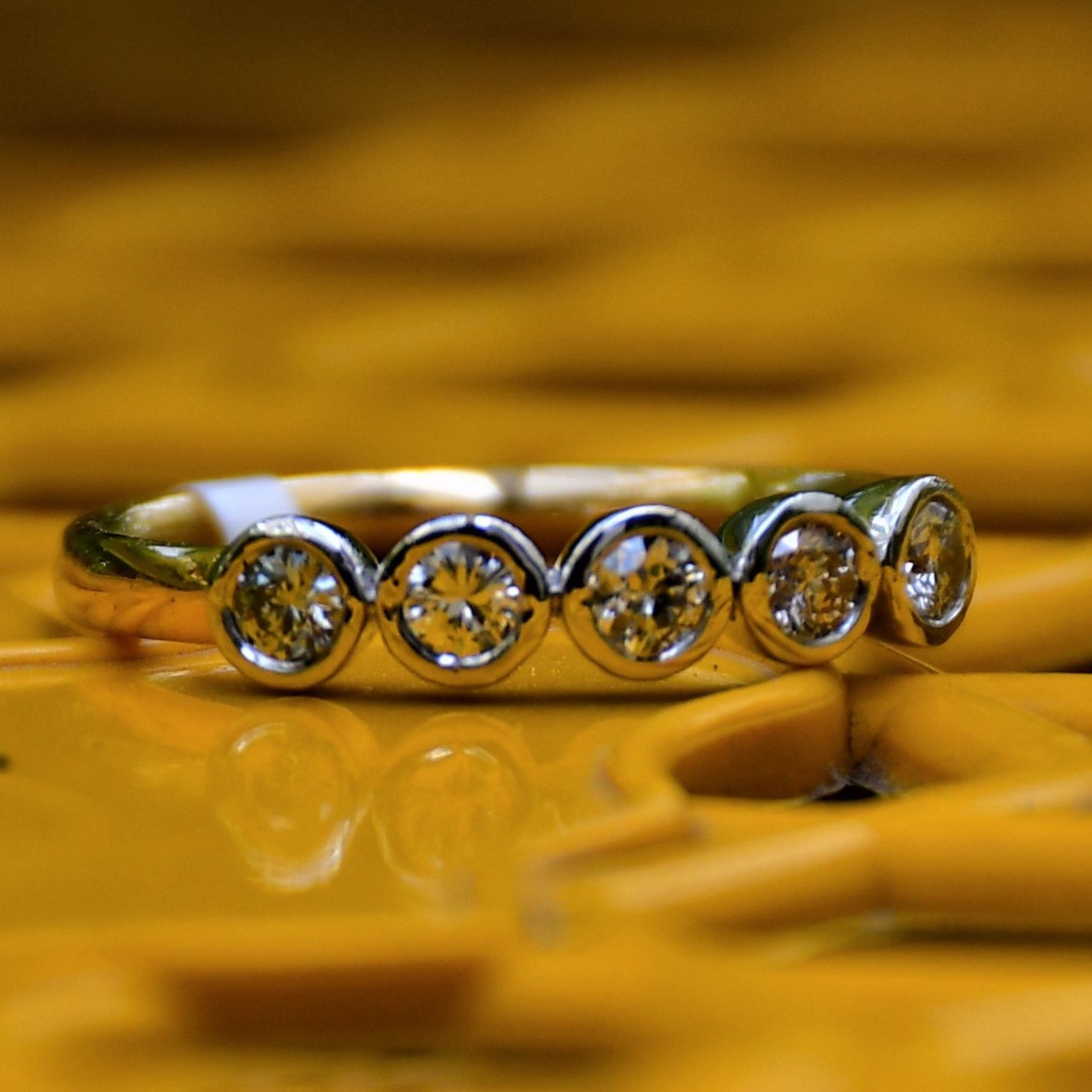 A yellow gold band ring with a series of set diamonds, featuring smaller diamonds, all set in a solid gold band displayed on a yellow color surface.