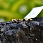 A 14kt gold diamond band ring with blue color stones, positioned on a rocky surface with green foliage in the background.