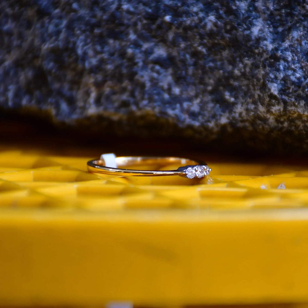 A 14kt gold diamond band ring with three brilliant cut natural diamonds on a yellow textured surface.