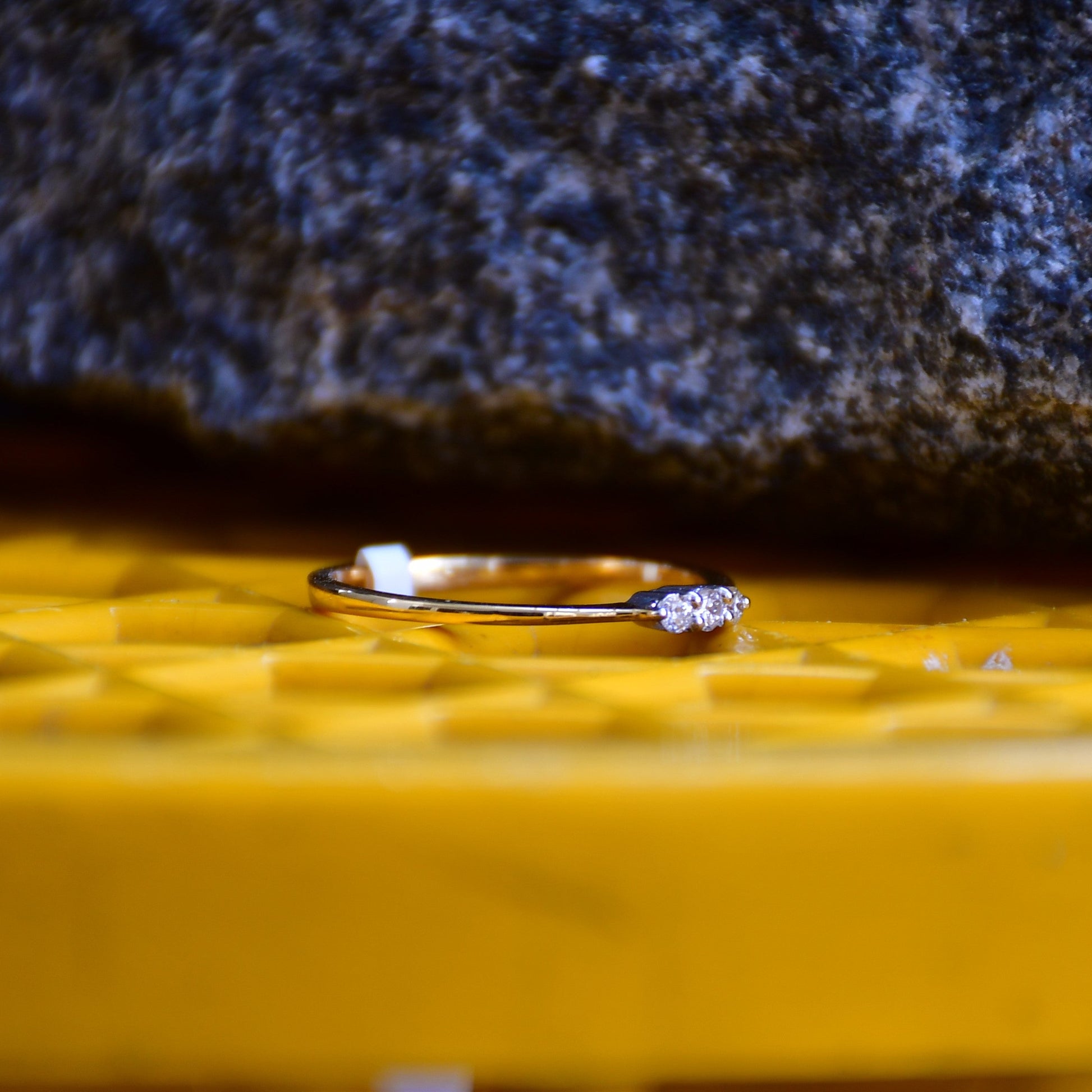 A 14kt gold diamond band ring with three brilliant cut natural diamonds on a yellow textured surface.