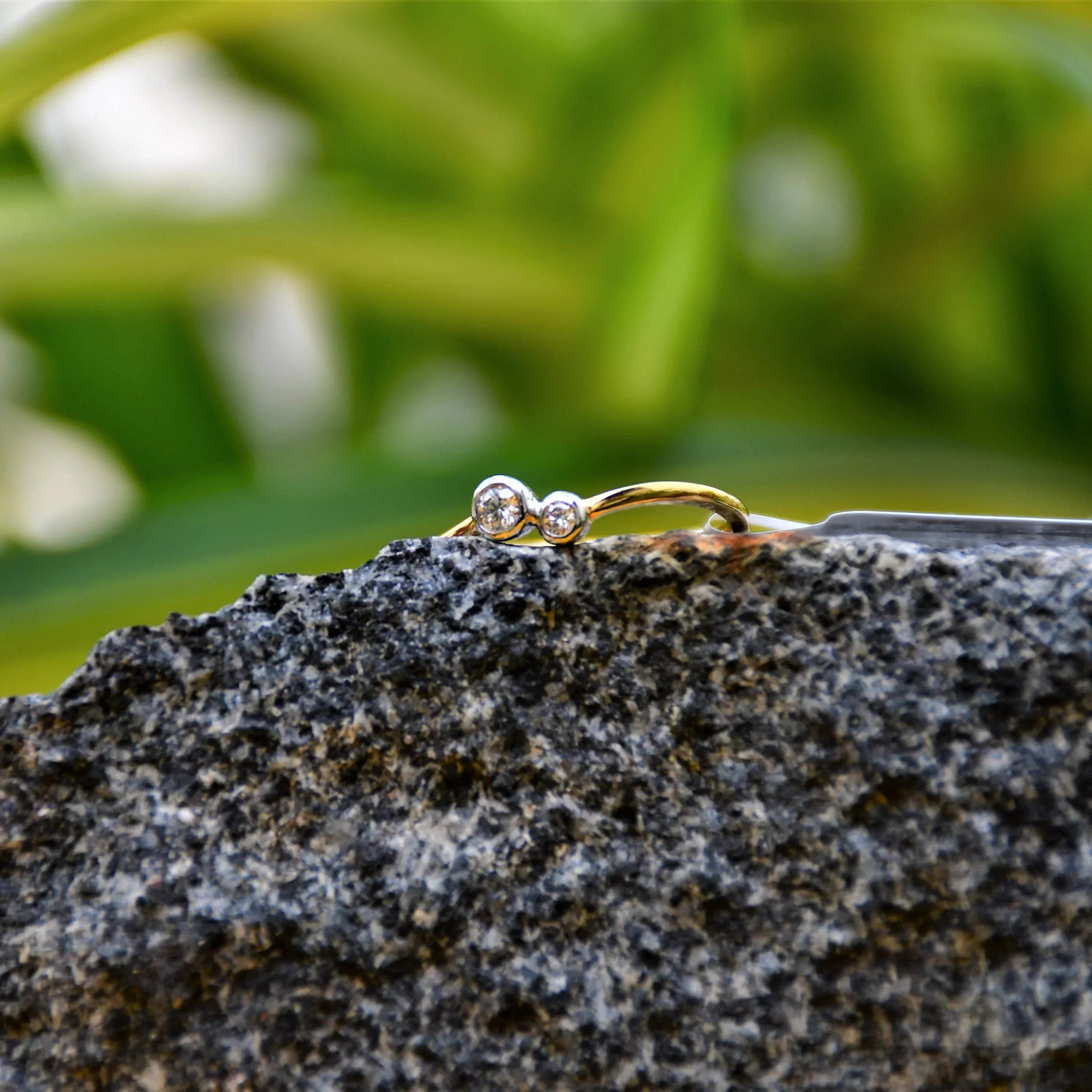 A 14kt gold band ring with two set diamonds on it, placed on rough textured stone surface.