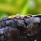 A 14kt gold band ring with two set diamonds on it, placed on a black rough surface.