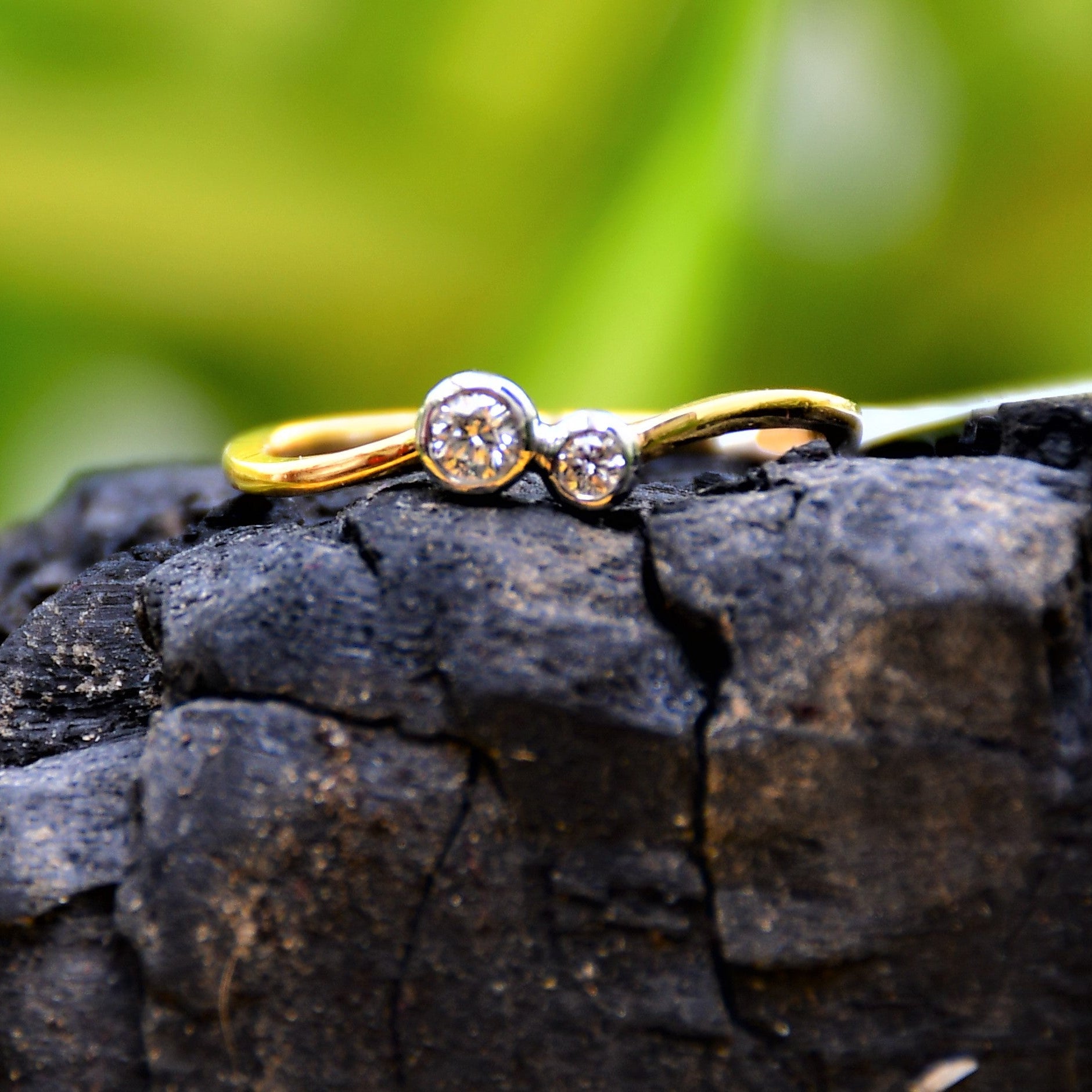 A 14kt gold band ring with two set diamonds on it, placed on a black rough surface.