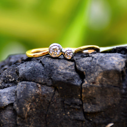 A 14kt gold band ring with two set diamonds on it, placed on a black rough surface.