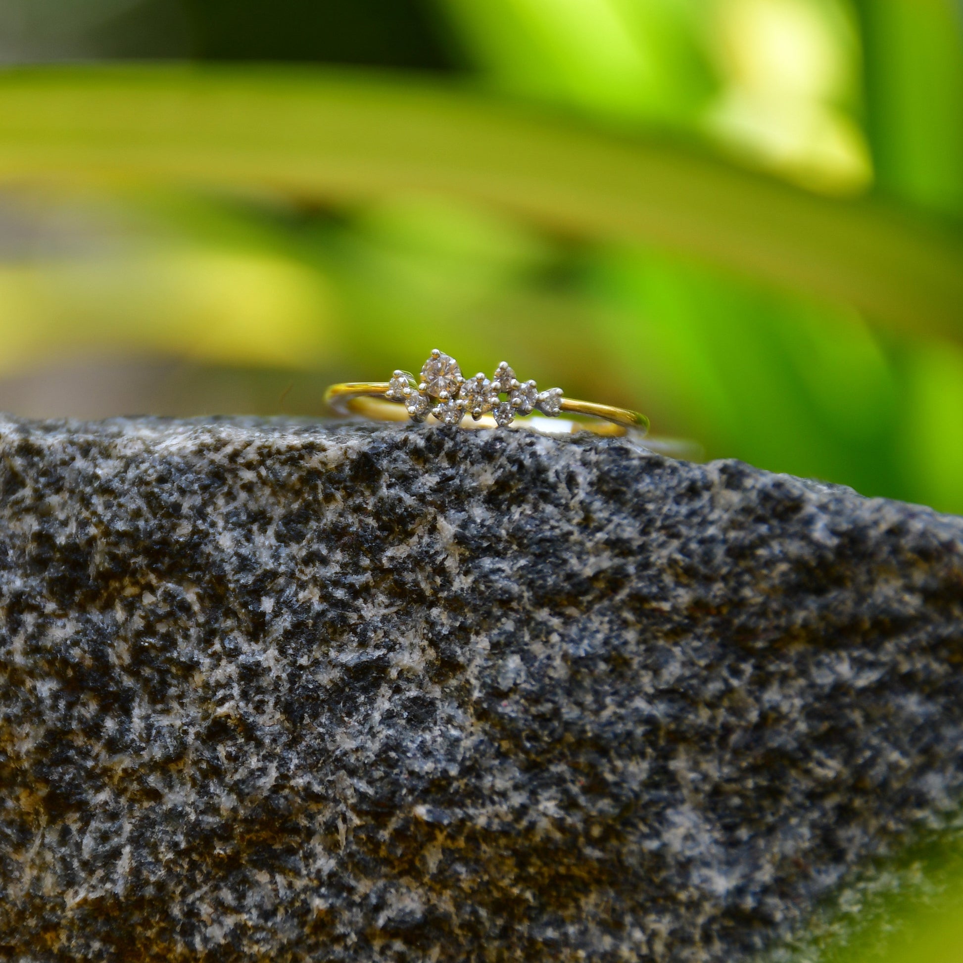 A gold diamond band ring set on a stone surface with a blurred green background.