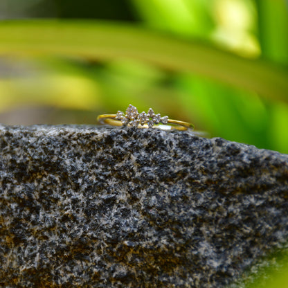 A gold diamond band ring set on a stone surface with a blurred green background.