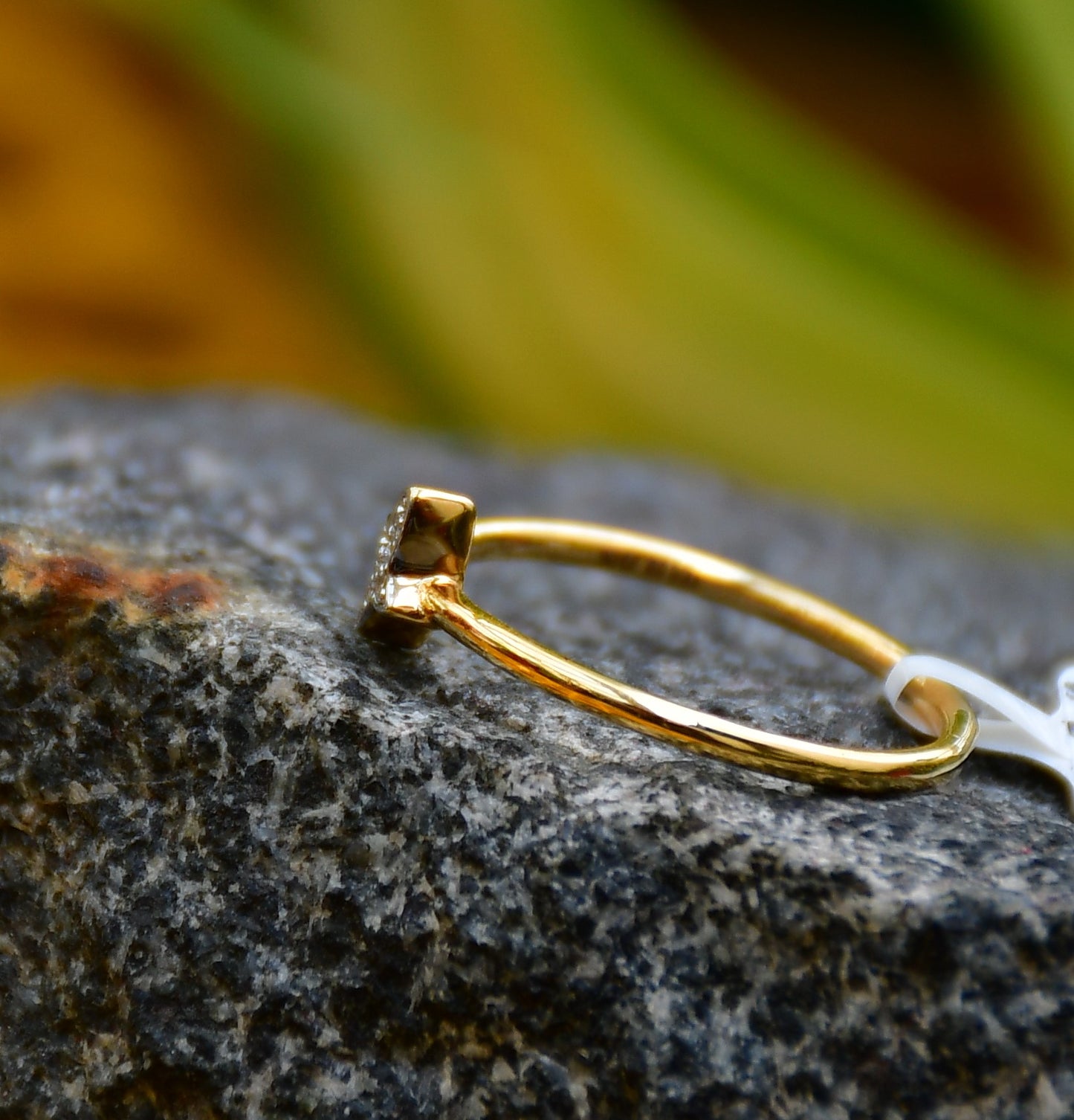 A gold diamond band ring with a butterfly-shape on a rocky surface.