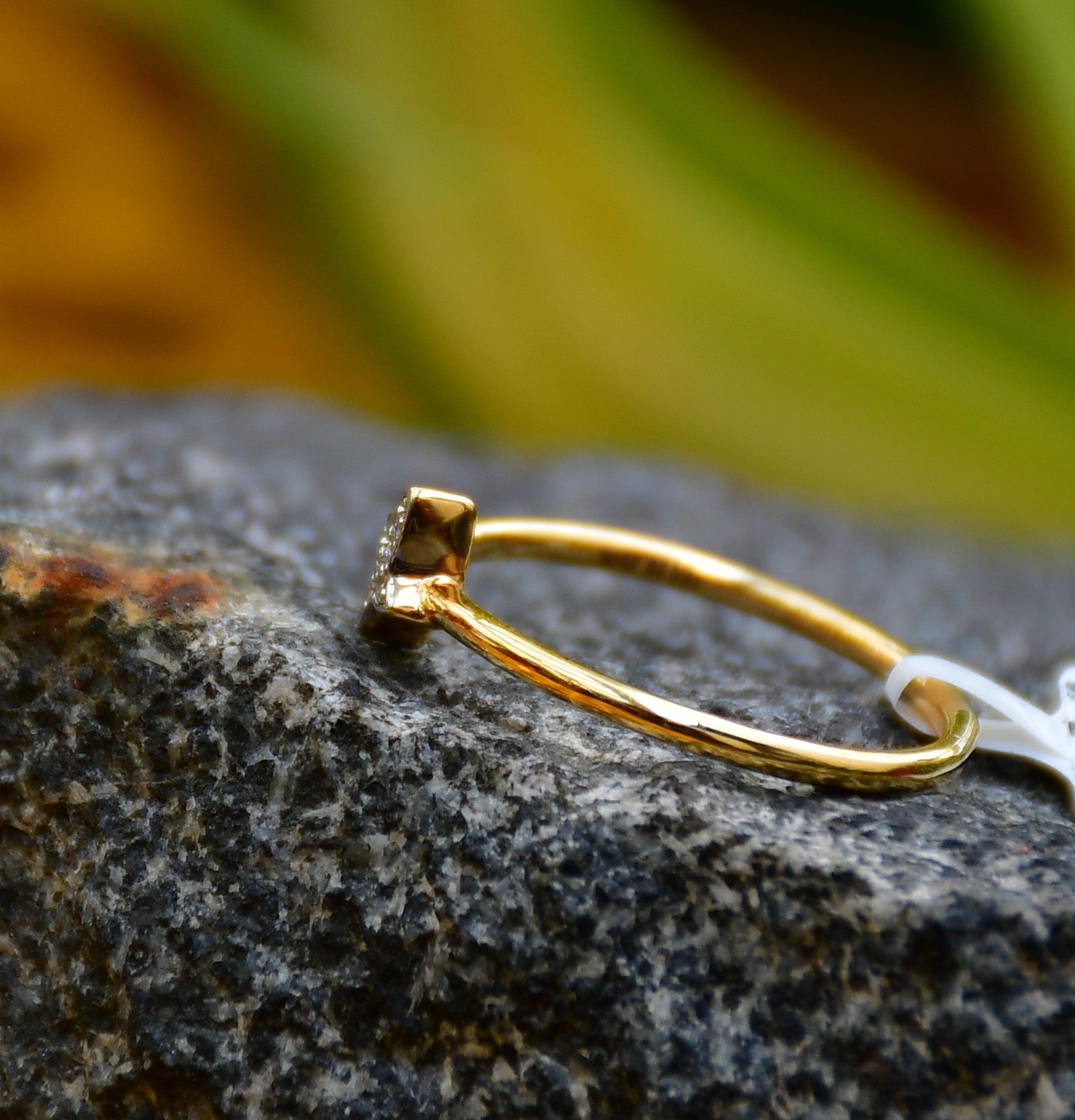 A gold diamond band ring with a butterfly-shape on a rocky surface.