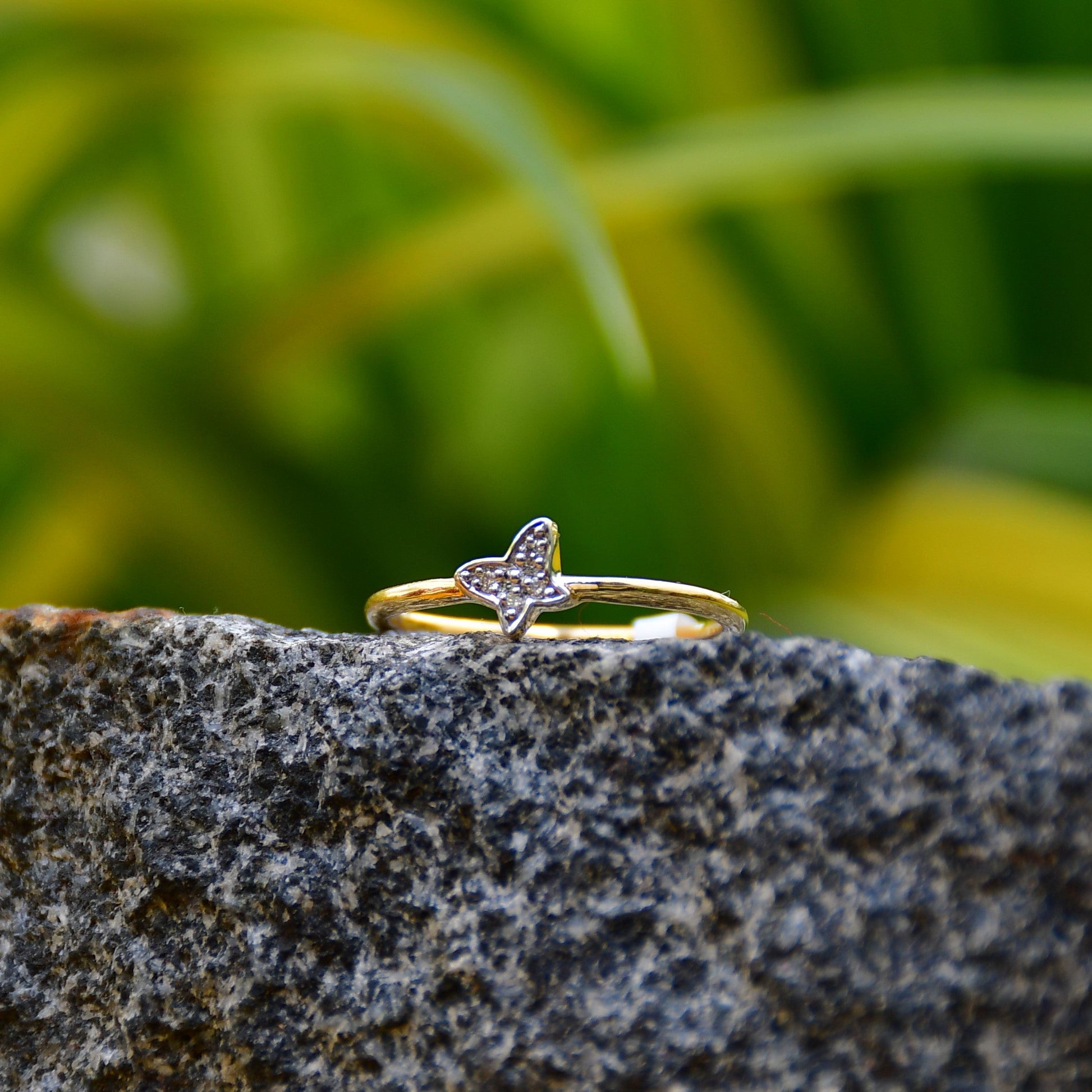 A gold diamond band ring with a butterfly-shape on a rocky surface.