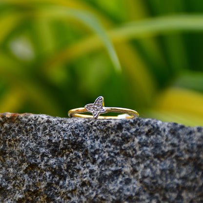 A gold diamond band ring with a butterfly-shape on a rocky surface.