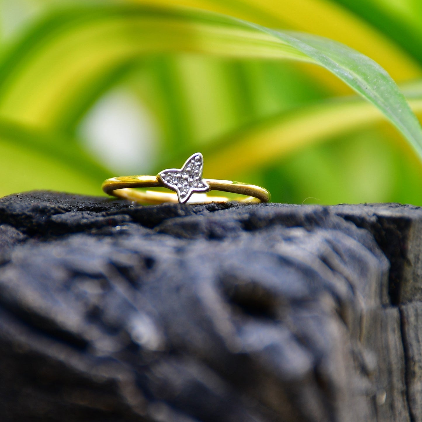 A gold diamond band ring with a butterfly-shape on a rocky surface.