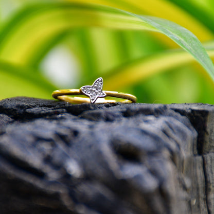 A gold diamond band ring with a butterfly-shape on a rocky surface.