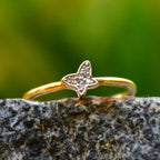 A gold diamond band ring with a butterfly-shape on a rocky surface.