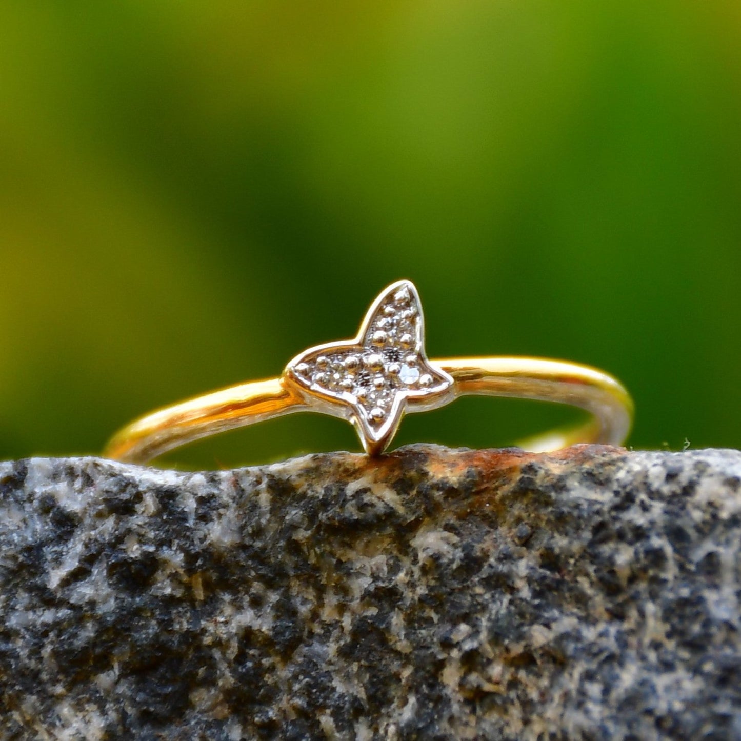 A gold diamond band ring with a butterfly-shape on a rocky surface.
