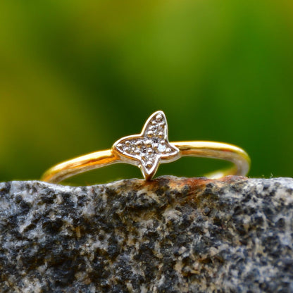 A gold diamond band ring with a butterfly-shape on a rocky surface.