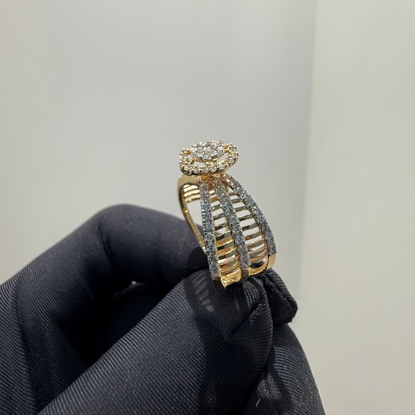 Elegant gold diamond ring featuring a round-cut central diamond surrounded by a halo of smaller diamonds, set on a split shank band adorned with rows of sparkling pavé diamonds, displayed on a black gloved hand against a neutral background.