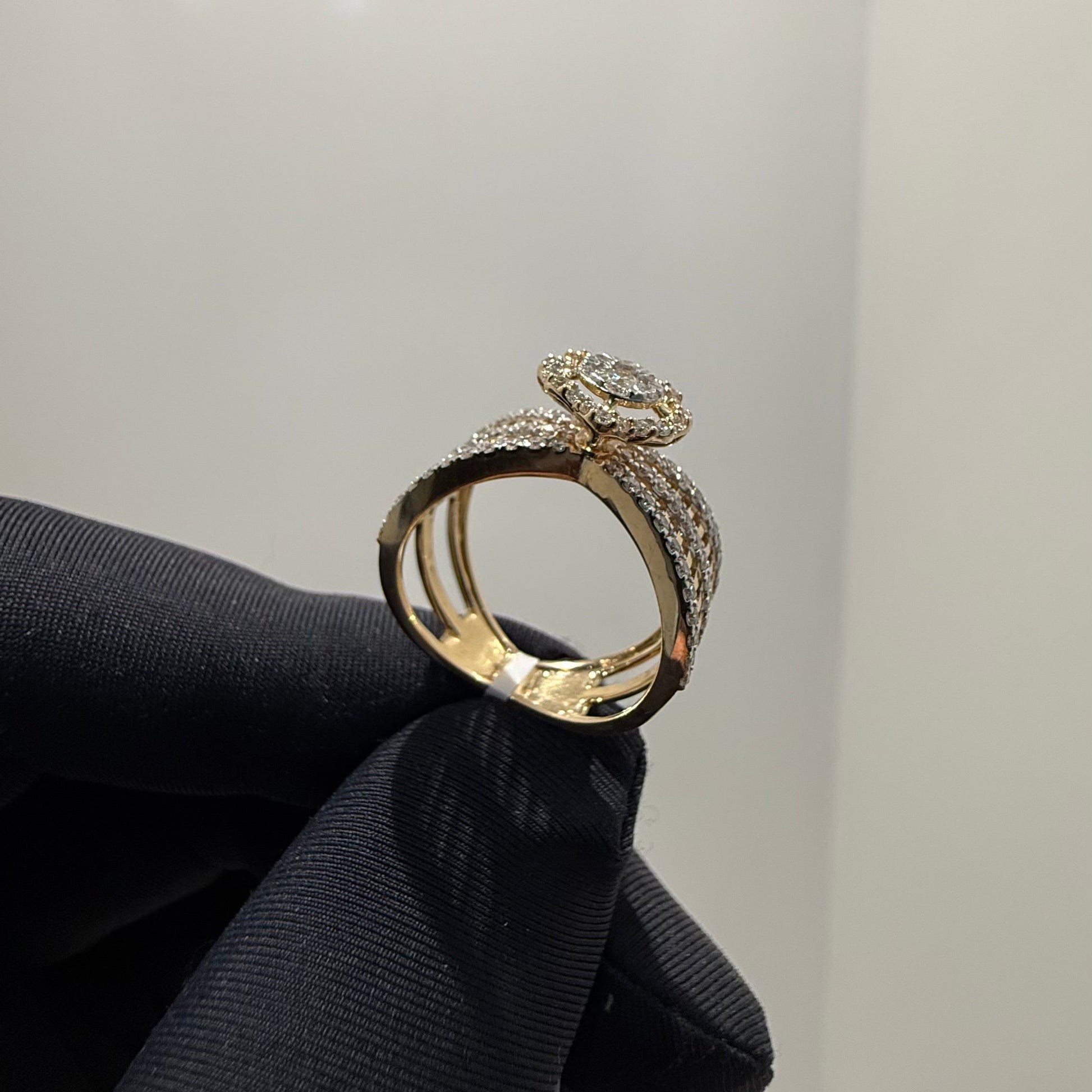 Elegant gold diamond ring featuring a round-cut central diamond surrounded by a halo of smaller diamonds, set on a split shank band adorned with rows of sparkling pavé diamonds, displayed on a black gloved hand against a neutral background.