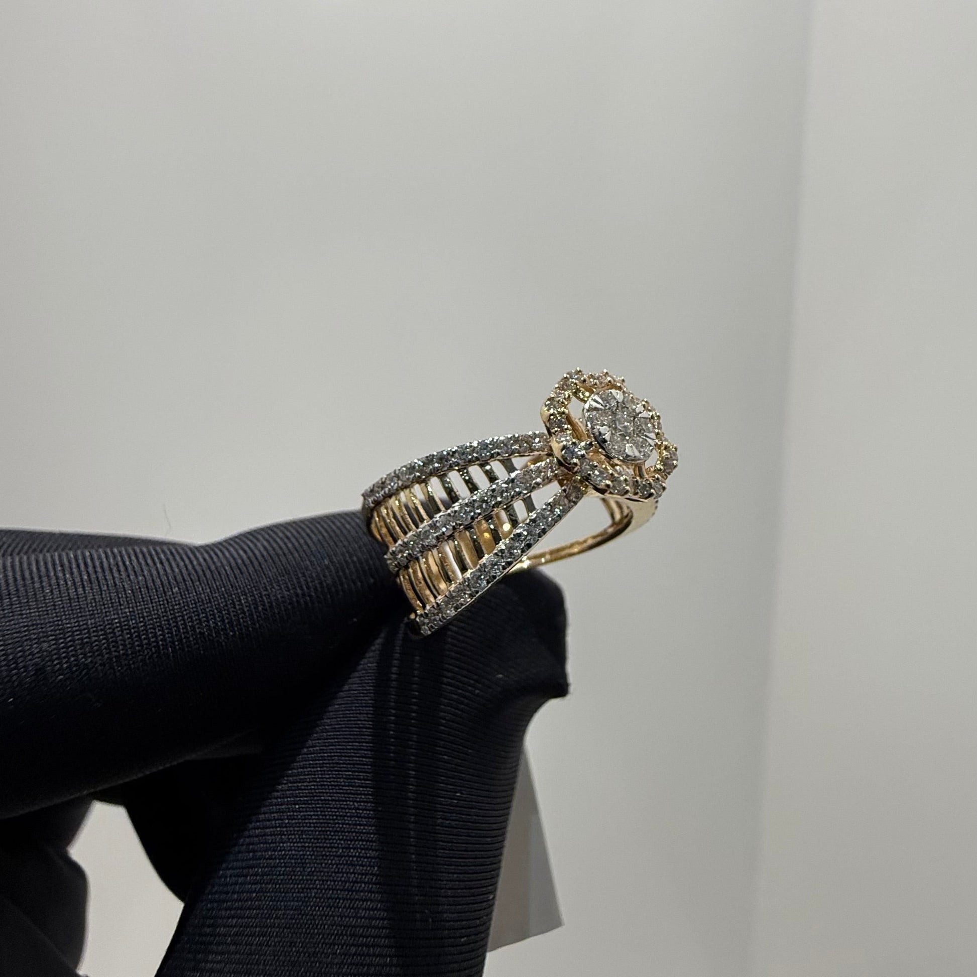 Elegant gold diamond ring featuring a round-cut central diamond surrounded by a halo of smaller diamonds, set on a split shank band adorned with rows of sparkling pavé diamonds, displayed on a black gloved hand against a neutral background.