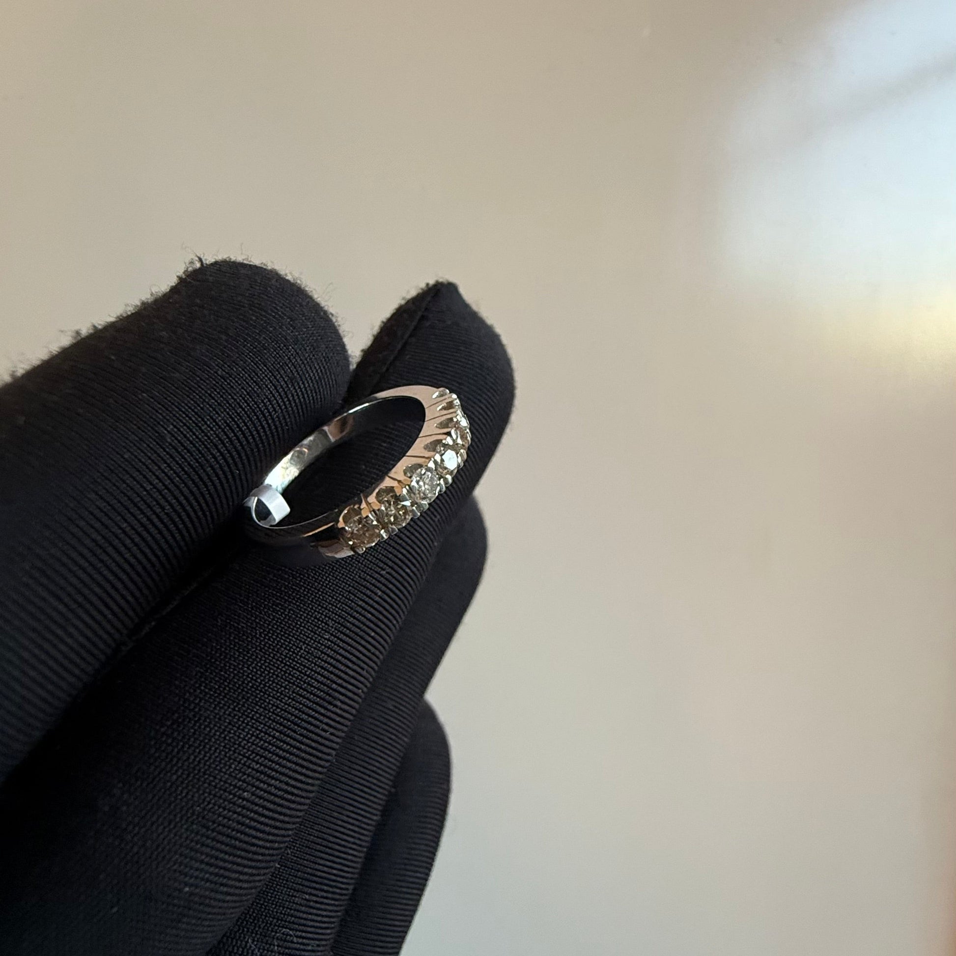 A band diamond ring with multiple stones set in a gold band, displayed on a black glove against a neutral background.