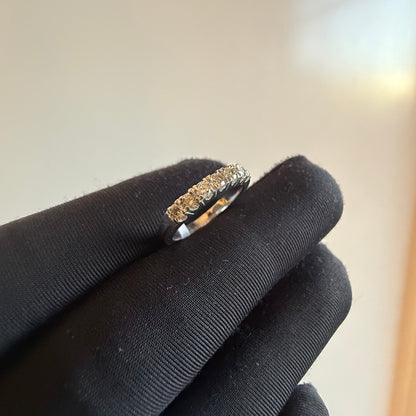 A band diamond ring with multiple stones set in a gold band, displayed on a black glove against a neutral background.