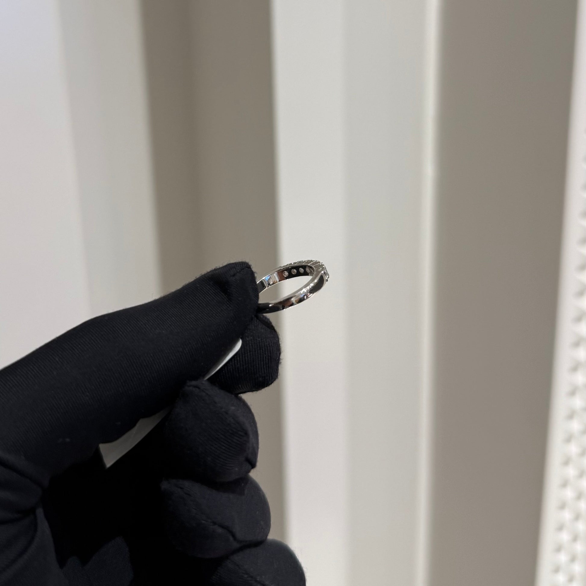 A band diamond ring with multiple stones set in a gold band, displayed on a black glove against a neutral background.
