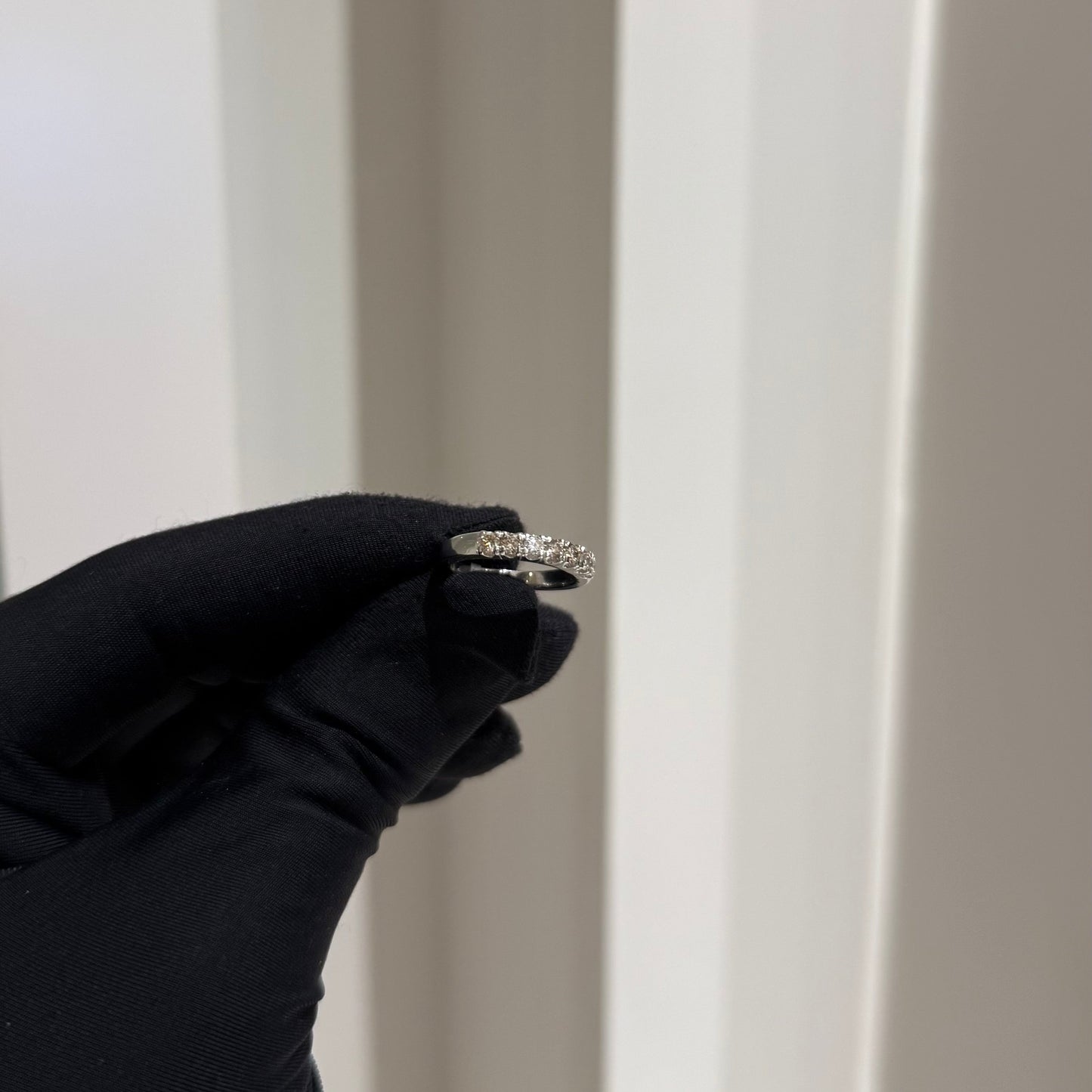 A band diamond ring with multiple stones set in a gold band, displayed on a black glove against a neutral background.