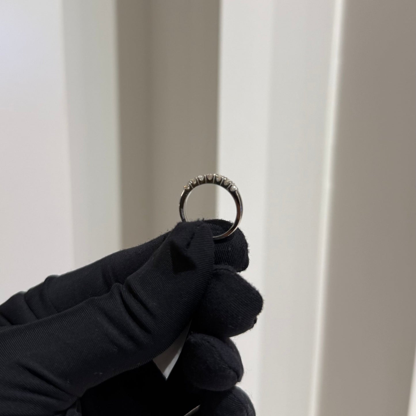 A band diamond ring with multiple stones set in a gold band, displayed on a black glove against a neutral background.