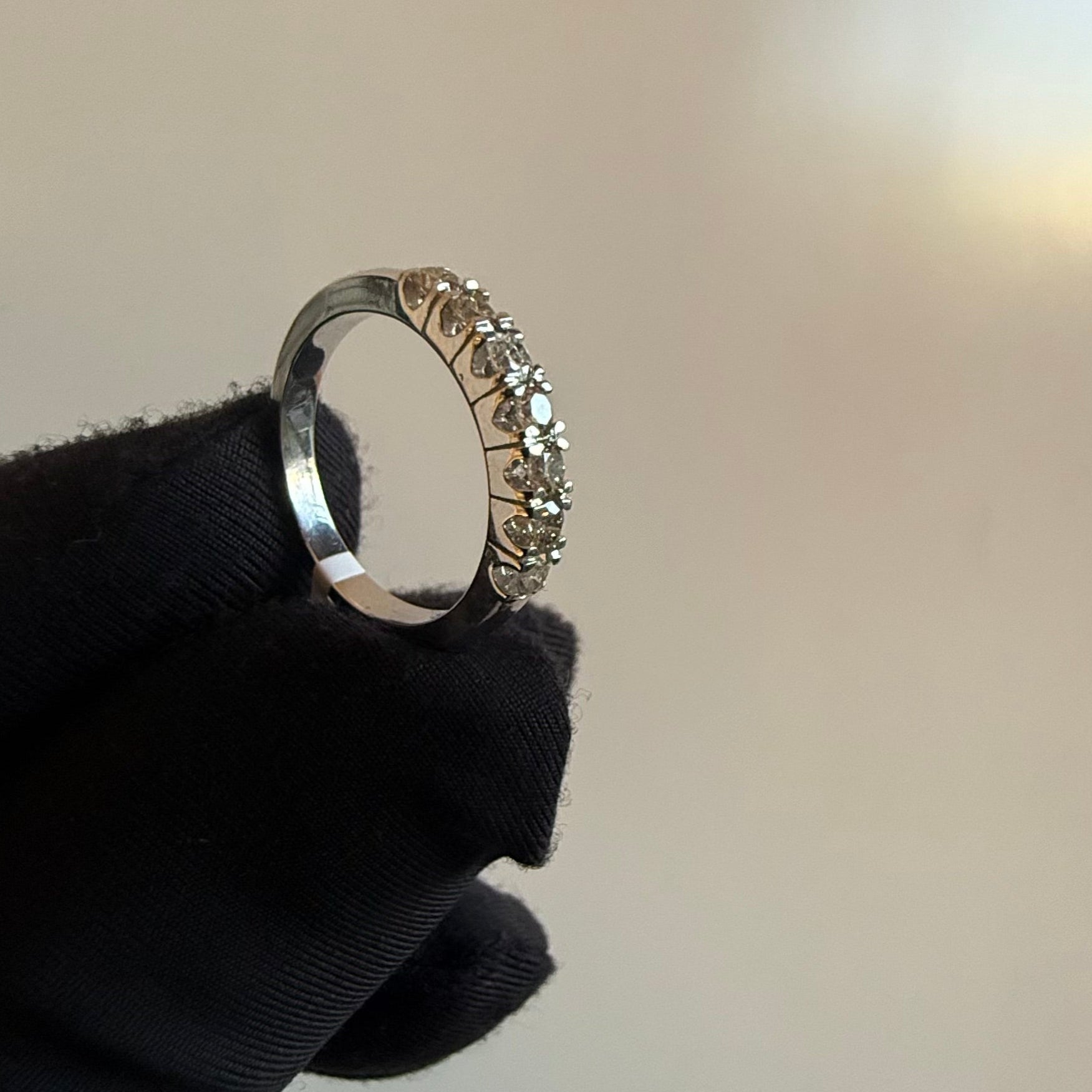 A band diamond ring with multiple stones set in a gold band, displayed on a black glove against a neutral background.