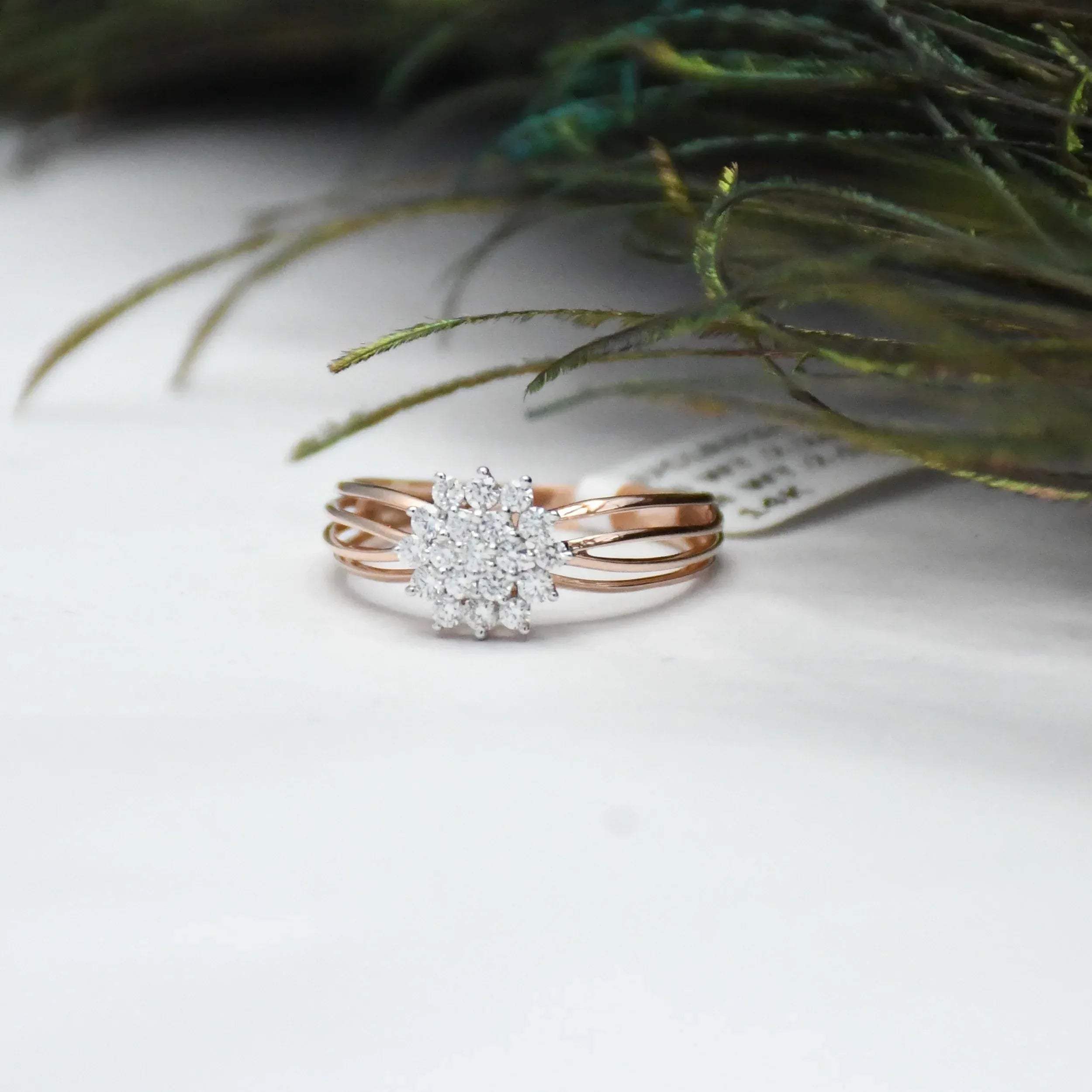 Rose gold ring with diamond accents on a white surface with greenery.