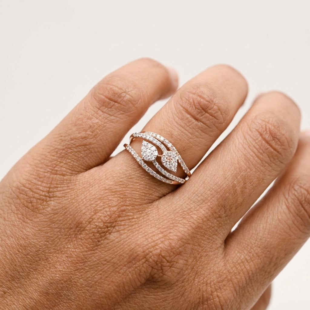 A close-up of a hand wearing a rose gold ring with pavé-set clear stones, including two pear-shaped center diamond cluster and curved bands.