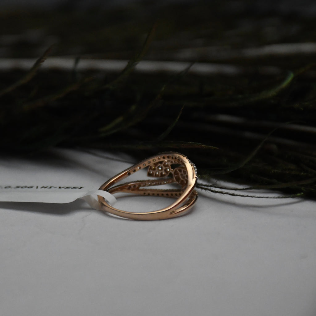 A rose gold ring with a textured, openwork design and a small central cluster of clear diamonds, resting on a white surface with a dark, blurred background.