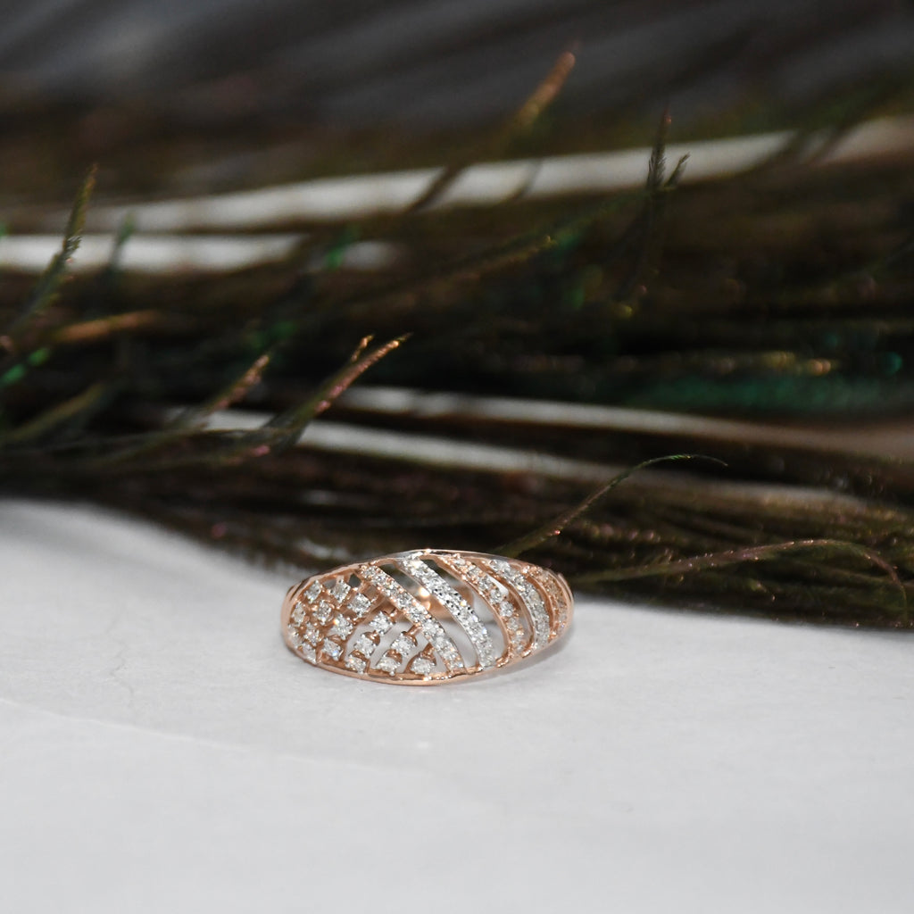 A rose gold ring with a textured, diamond patterned band, resting on a white surface with dark feathers in the background.