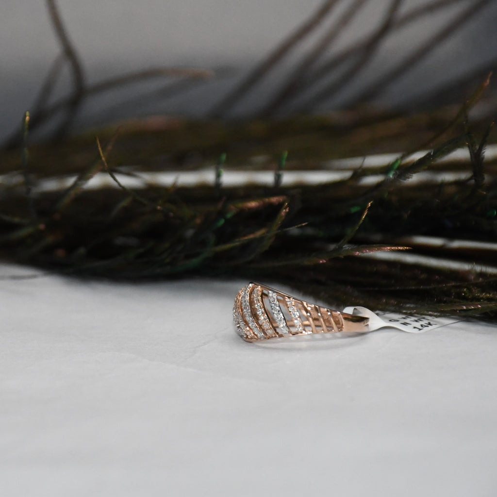 A close-up of a small jewelry piece with a rose-gold curved setting and clear diamonds, resting on a white surface with dark hair strands blurred in the background.
