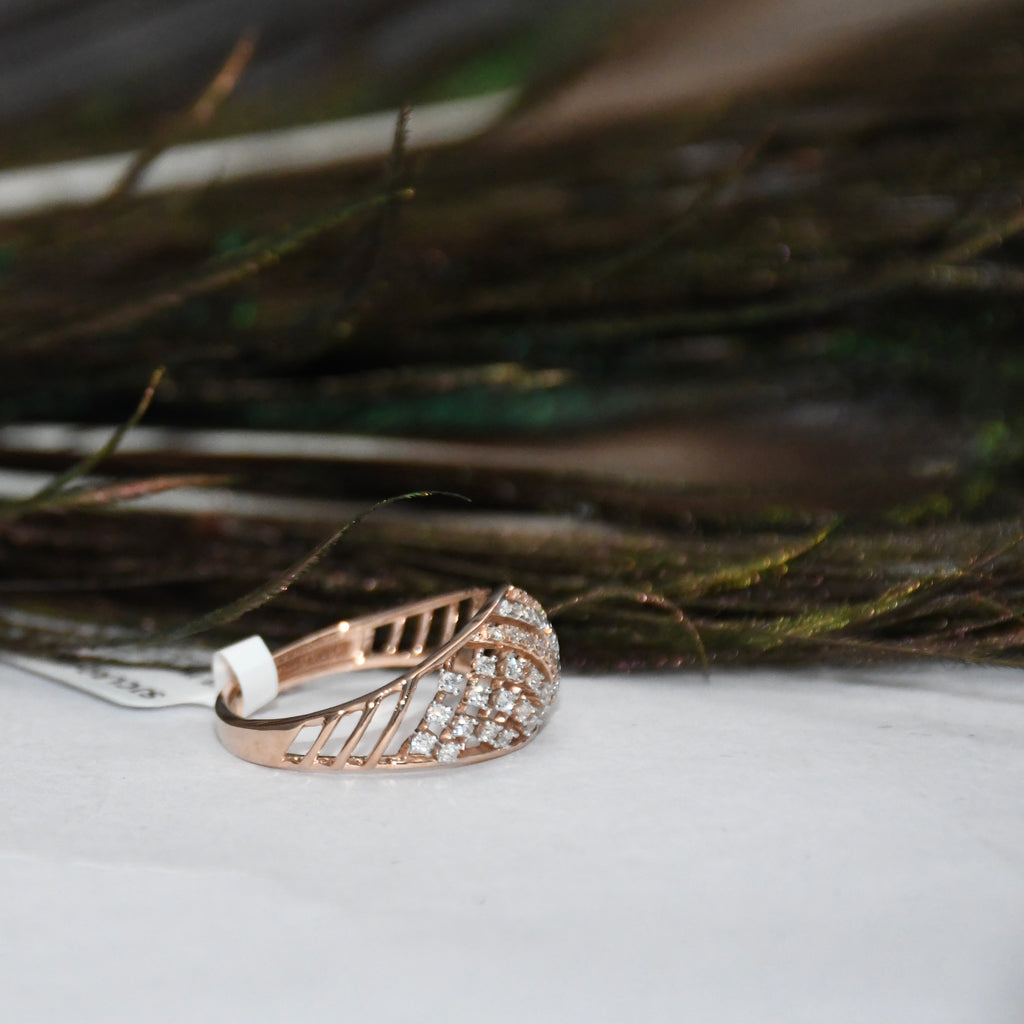 A rose gold ring with a leaf-shaped pavé setting and clear diamonds, resting on a white surface with a blurred natural background.