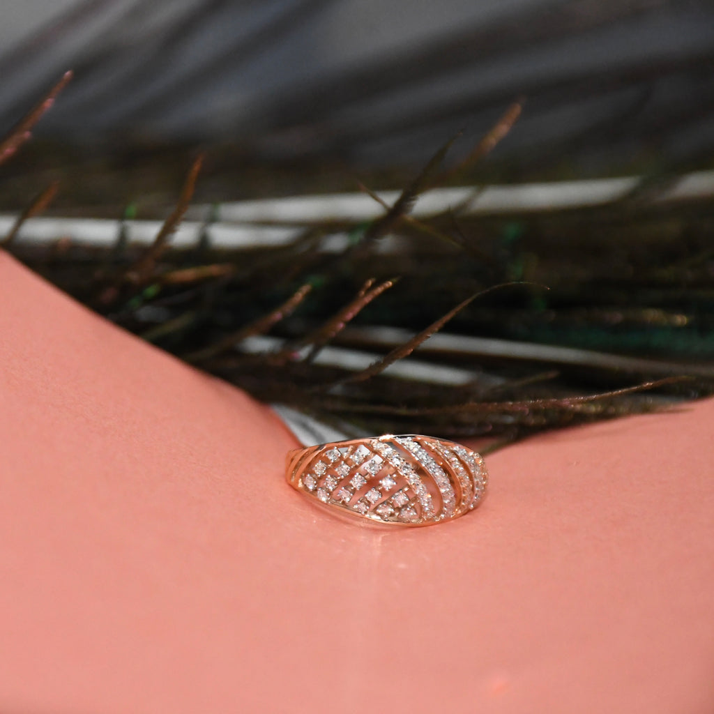 A rose gold ring with a pavé diamond design, resting on a pink surface with dark feathers in the background.