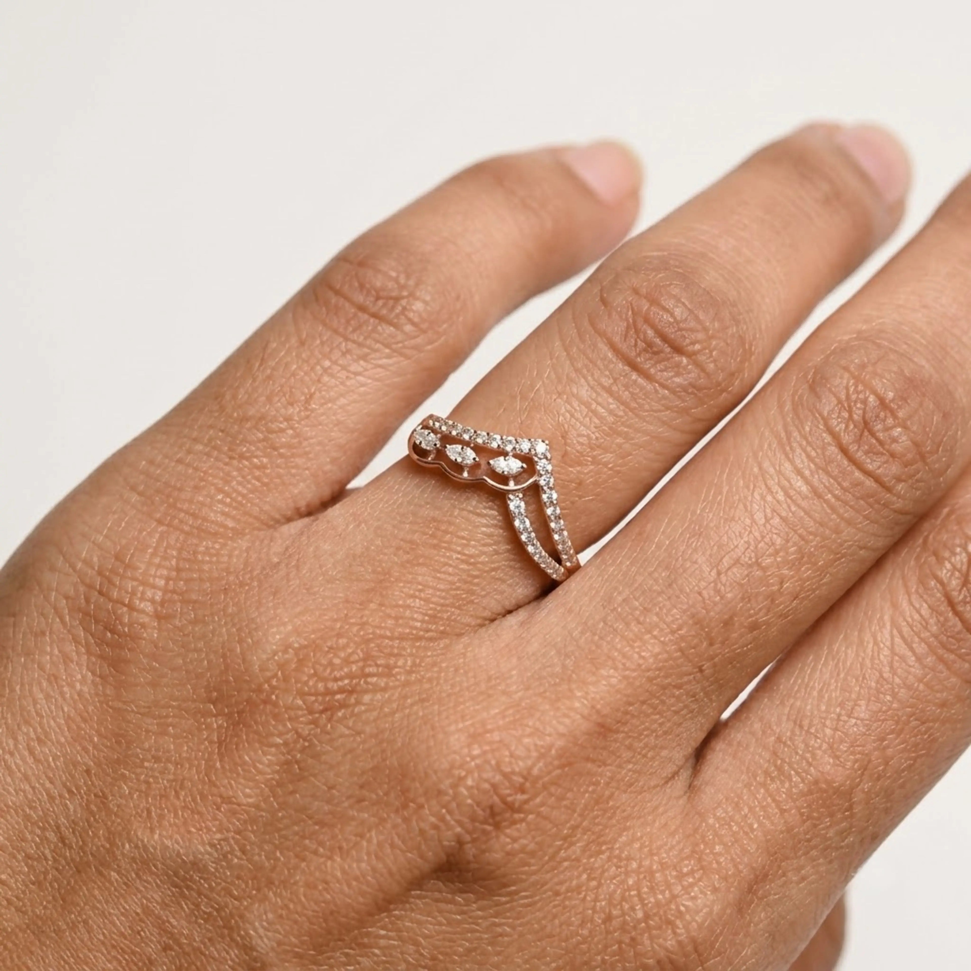 A close-up of a hand wearing a delicate rose gold ring with small clear diamonds, set against a plain light background.