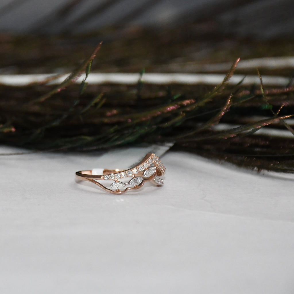 A rose gold ring with pavé-set clear stones, photographed on a white surface with dark feathers in the blurred background.
