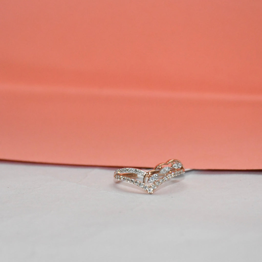 A delicate rose gold ring with pavé-set clear stones, photographed on a white surface with a peach-pink background.