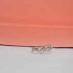 A delicate rose gold ring with pavé-set clear stones, photographed on a white surface with a peach-pink background.
