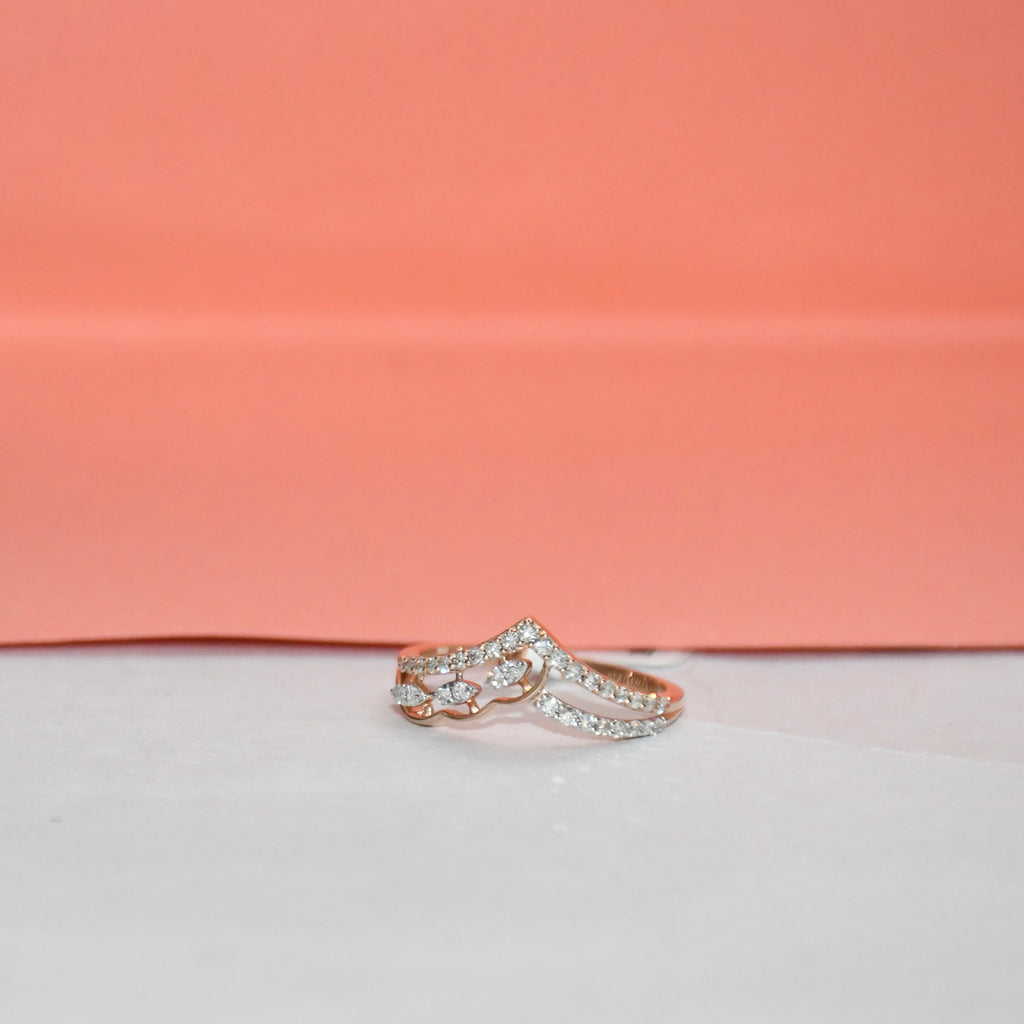 A rose gold ring with pavé-set clear stones, photographed on a white surface with a peach-pink background.